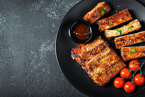 Hot grilled spare ribs from a summer BBQ served on a plate with sauce. Top view, a Food & Drink Photo by Budarinphoto