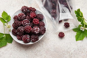Frozen blackberries spilling from a bag into a bowl, a Food & Drink Photo by Olena Rudo