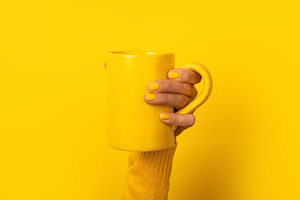 Close-up of a female hand with yellow nails holding a yellow mug, a Food & Drink Photo by Ales Munt