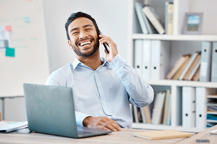 Happy businessman on a phone call while working on a laptop at the desk in his modern office. Corporate, professional and company manager laughing while having a mobile conversation with technology., a Photo by Peopleimages.com