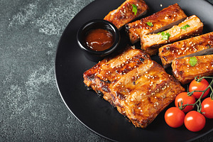 Hot grilled spare ribs from a summer BBQ served on a plate with sauce. Top view, a Food & Drink Photo by Budarinphoto
