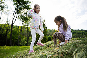 Two young girls enjoying a playful time in a lush green outdoor setting, a Person Photo by AS photostudio