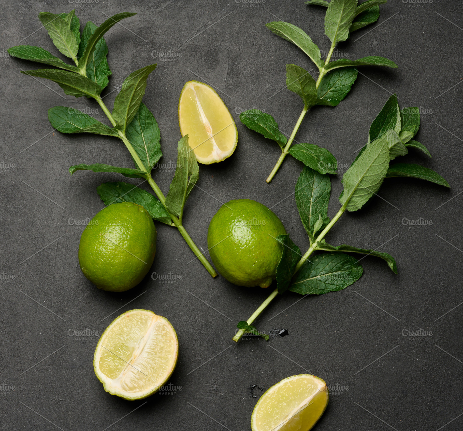 Whole and cut limes with fresh mint leaves arranged on a dark te, a Food & Drink Photo by ndanko