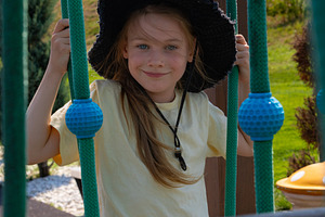 Cheerful young girl in a sun hat plays on outdoor playground ropes, enjoying a, a Person Photo by Ales Munt