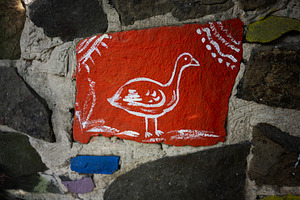 Hand-painted red stone art depicting a bird against a textured wall, a Photo by AS photostudio