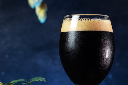 Glass of beer stout on a dark blue background, green hops