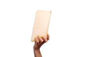 Large wedge of cheese held in a woman's hand with yellow nails,, a Food & Drink Photo by Ales Munt