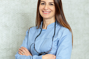 Portrait of smiling female dentist with arms crossed wearing surgical loupes, a Health & Medical Photo by Antonio Gravante Market
