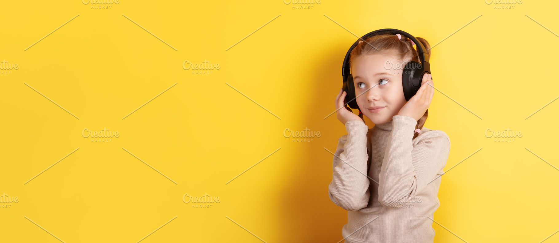 Smiling young girl wearing headphones against bright yellow back, a Person Photo by Ales Munt