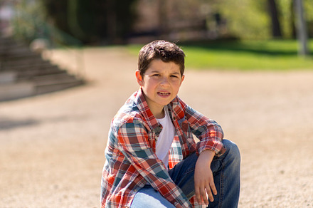 Young boy squatting on a gravel path in a sunny park., a Person Photo by RF Images