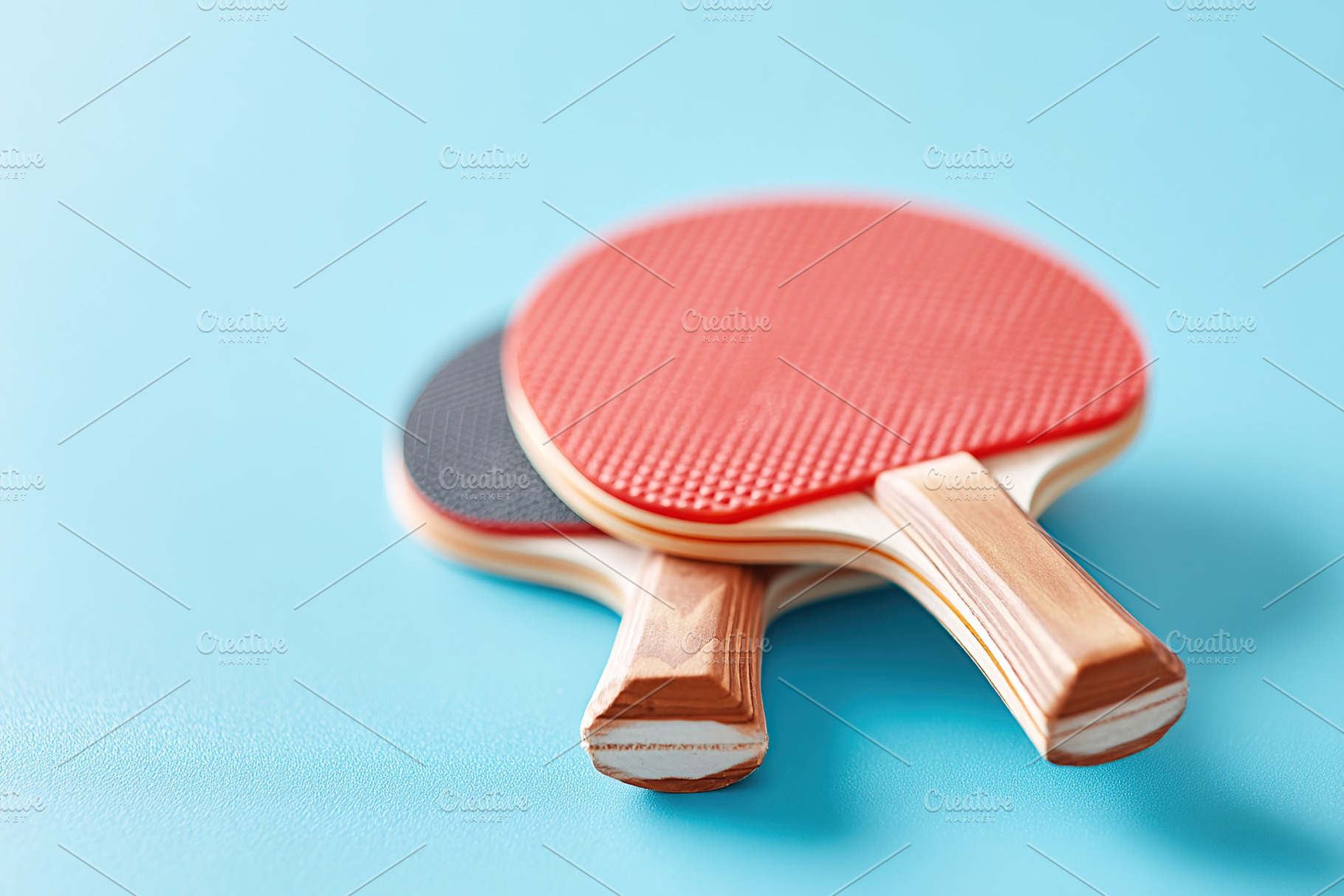 Two ping pong paddles resting on a blue surface ready for a game, a Photo by AlyaAnd