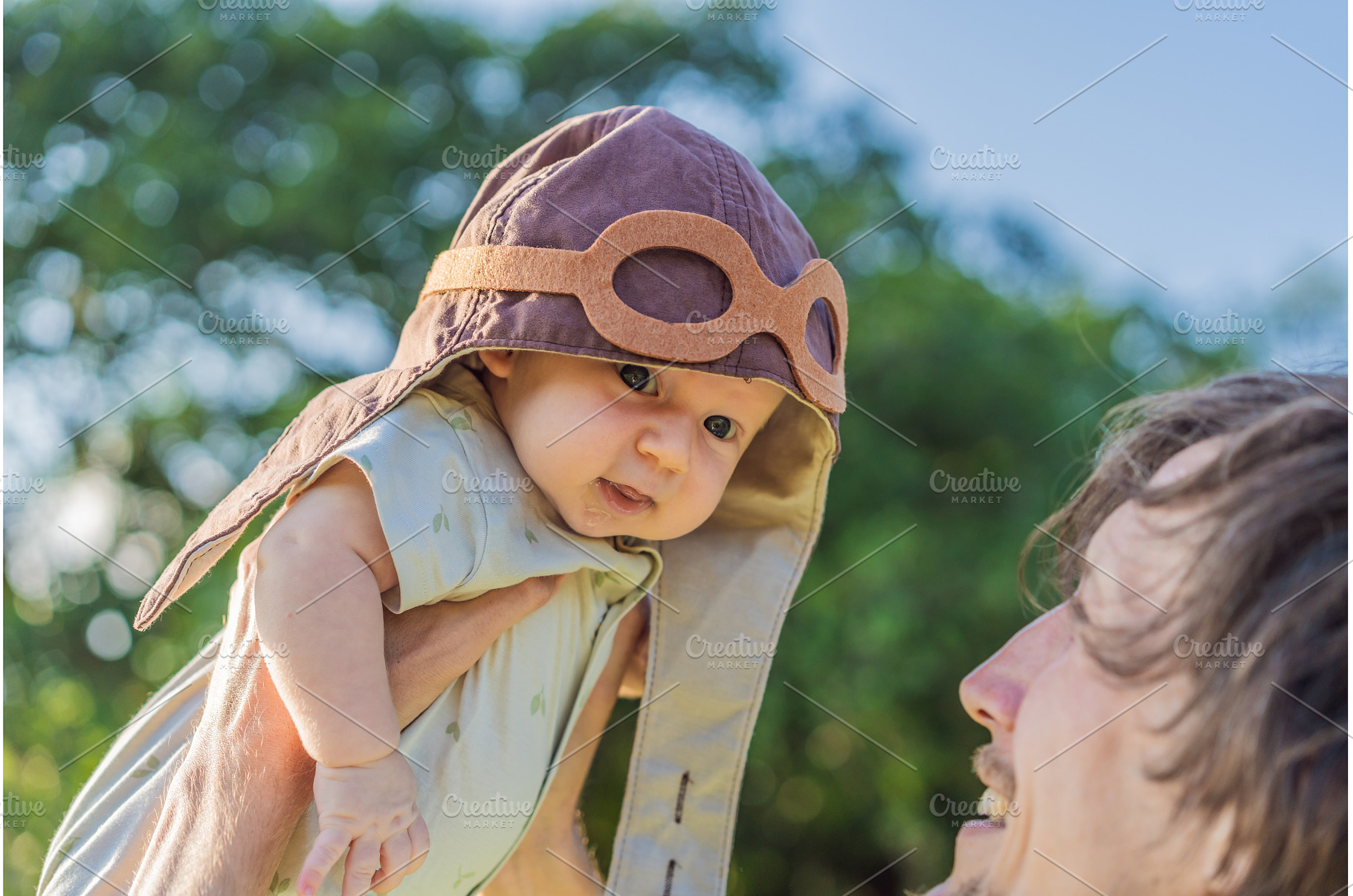 Father lifting baby in a pilot hat, a Person Photo by Elizaveta Galitskaya