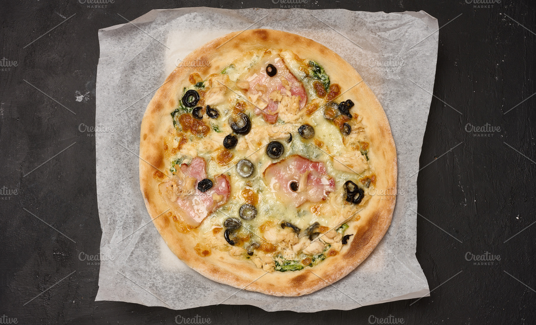 Round pizza with bacon, chicken, olives and cheese on parchment, a Food & Drink Photo by ndanko