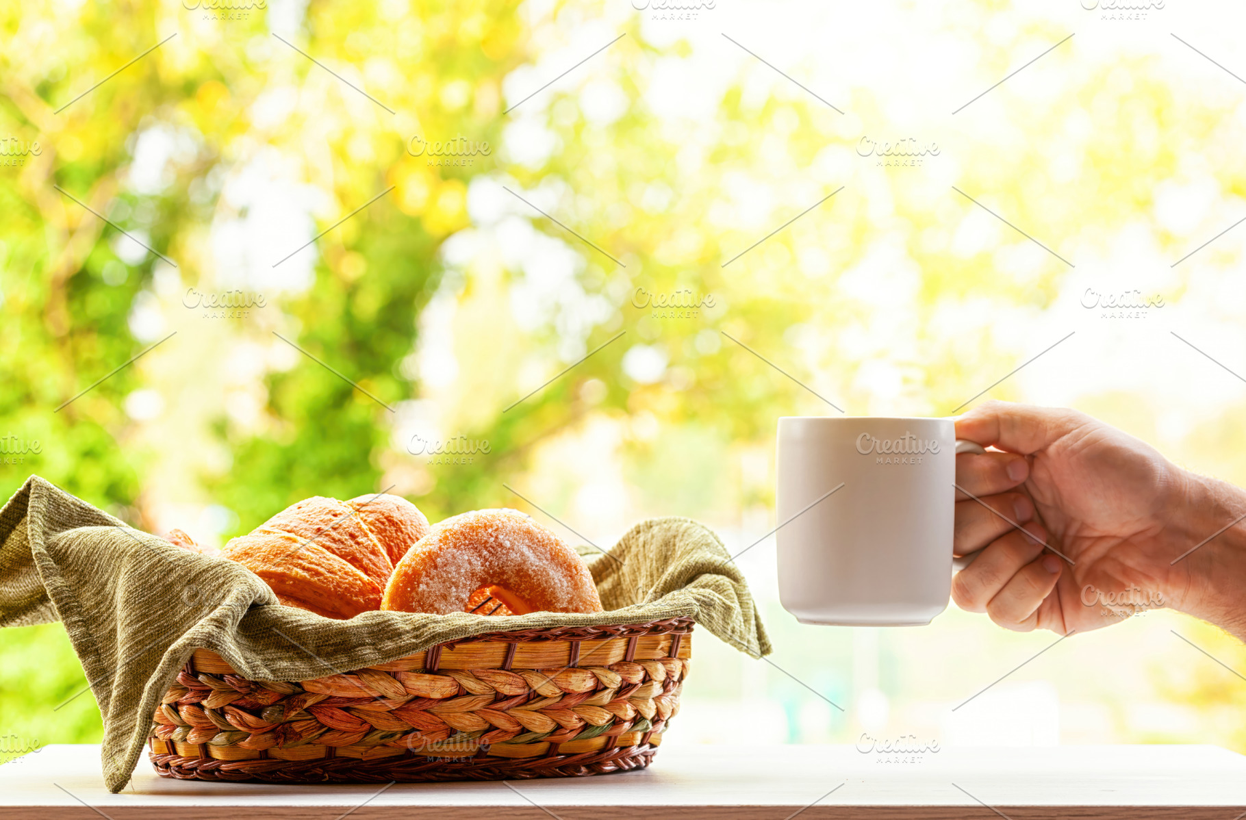 Hand holding coffee mug with basket of pastries and autumn foliage in backgroun, a Food & Drink Photo by Antonio Gravante Market