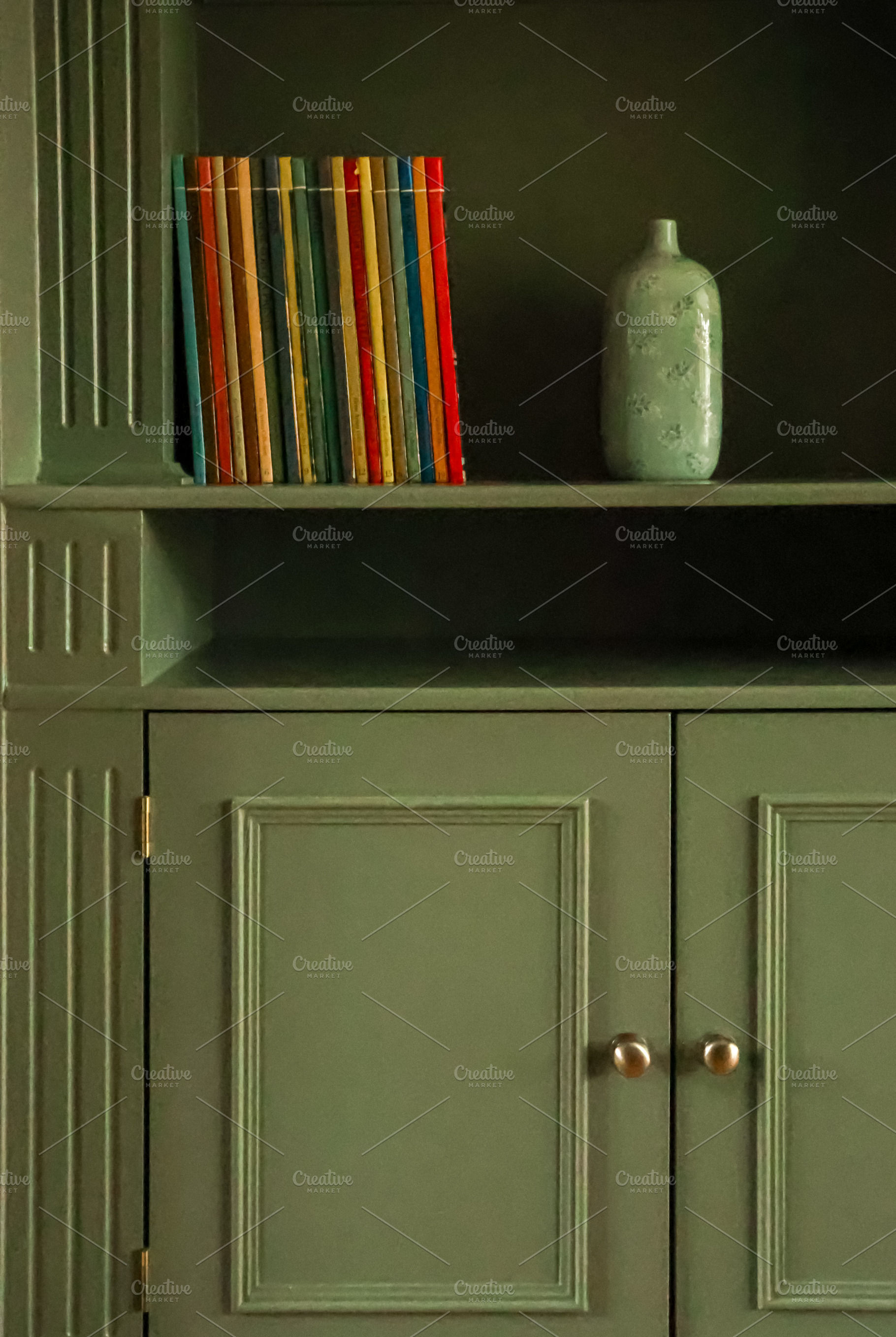 Bookshelf with colorful book spines and a vintage vase on a green wooden cabine, a Photo by Studio ANNA