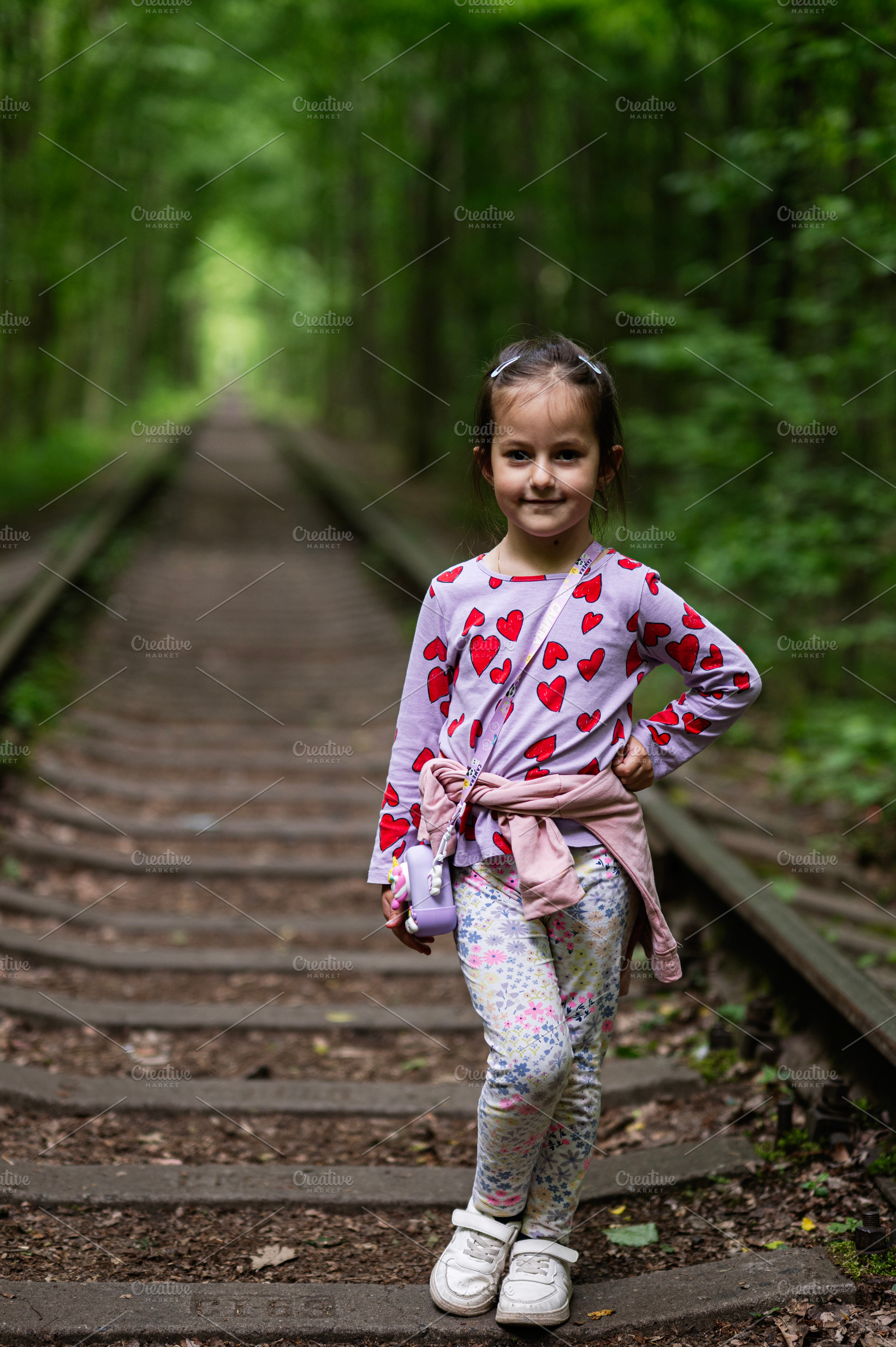Young girl posing confidently in a scenic forest trail with railway tracks, a Photo by AS photostudio