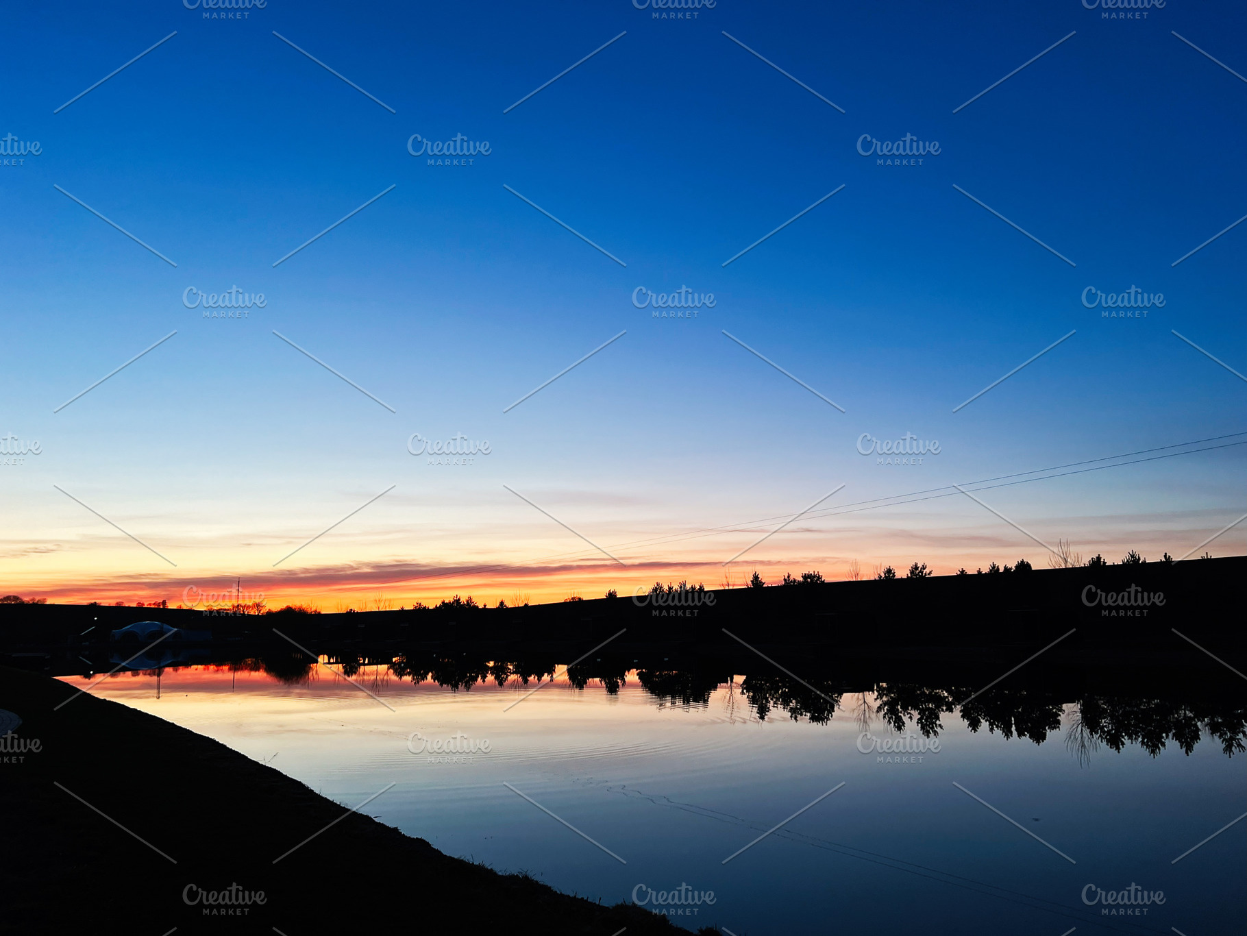 Serene sunset over a calm lake with trees and reflections, a Photo by AS photostudio