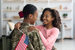 Cheerful girl with flag of the US hugging her mom, a Photo by Prostock-Studio