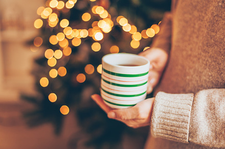 Female hand holding a mug of tea against the background of a Christmas tree wit