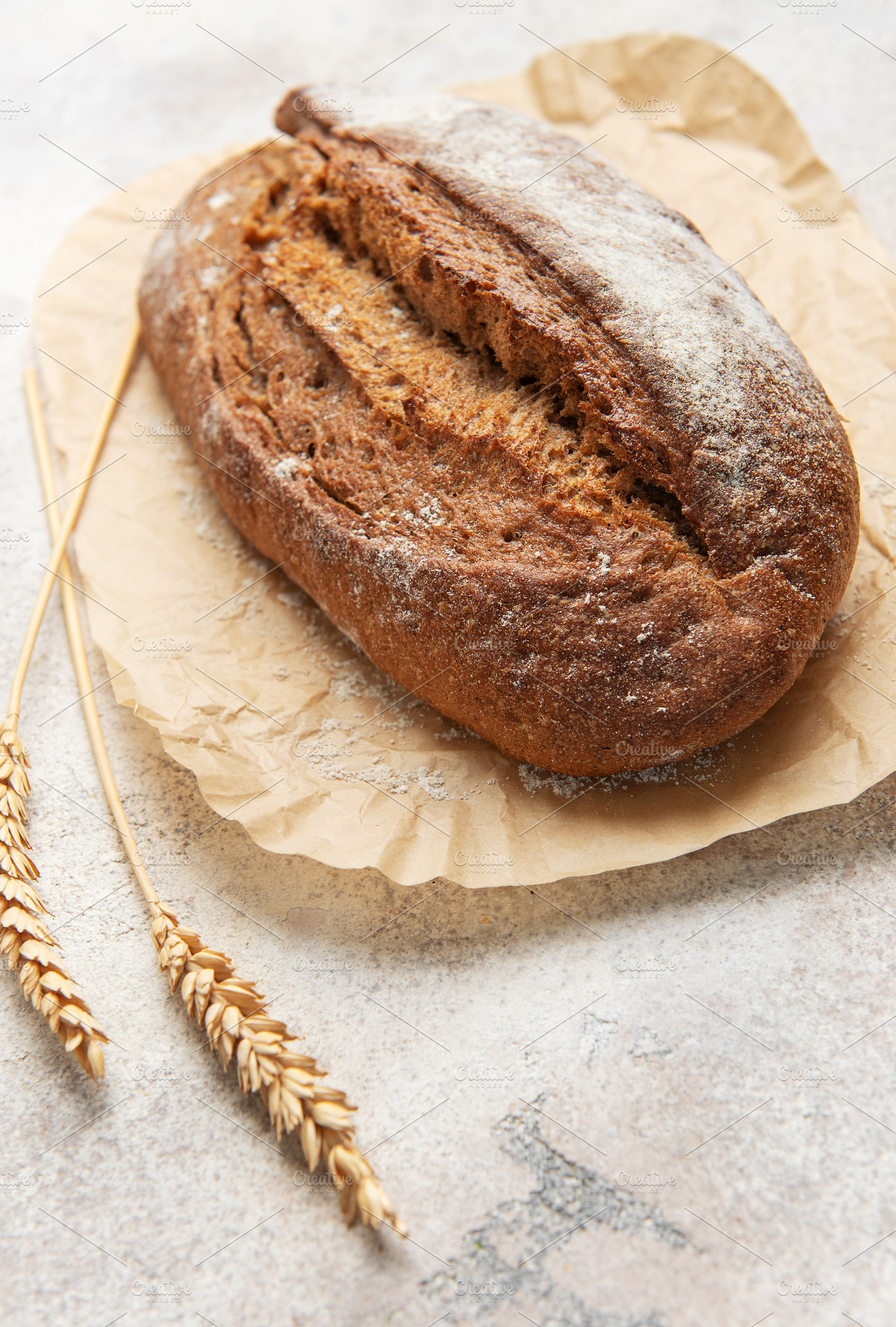 Rye bread loaf with wheat ears on parchment paper, a Food & Drink Photo by Olena Rudo