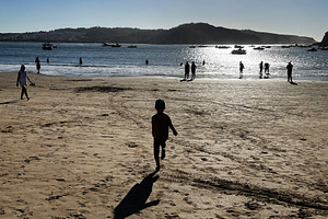 Silhouetted figures walk along a sunny beach by the calm water, a Photo by AS photostudio
