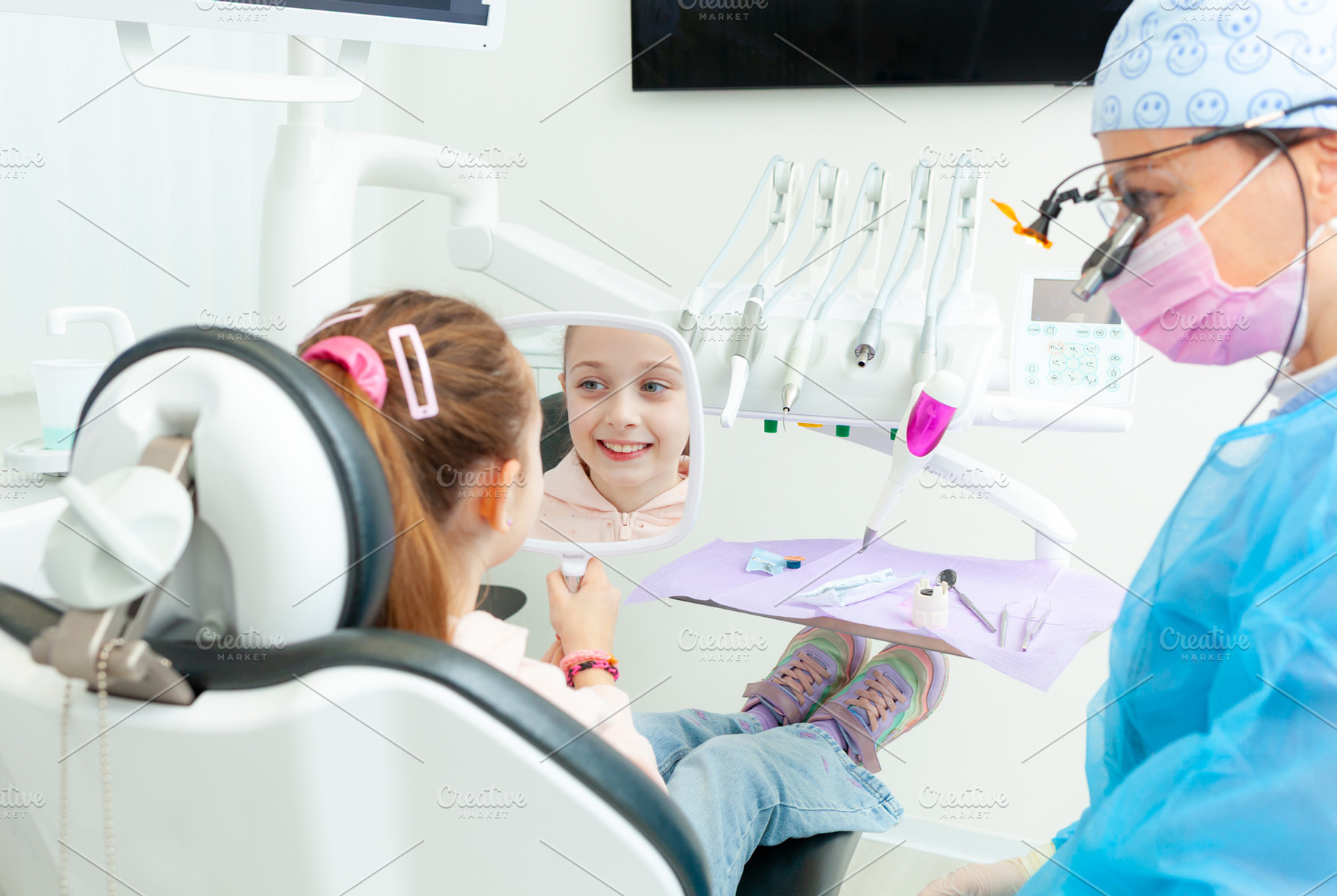 Little girl looking at her smile in the mirror at the pediatric dentist, a Photo by Antonio Gravante Market