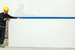 Construction worker holding large white plasterboard sheet in a construction si, an Industrial Photo by Antonio Gravante Market