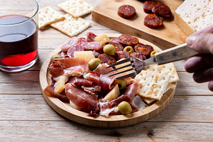 Fork picking up serrano ham from Spanish charcuterie board, a Food & Drink Photo by etorres69