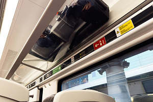 Travelers luggage stored overhead in modern train carriage with safety signs an, a Photo by AS photostudio