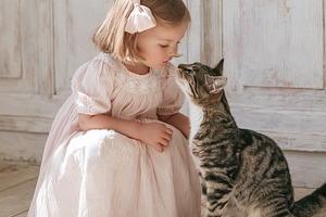 Little girl in striped dress bonding with a tabby cat, showing f, a Person Photo by Studio ANNA