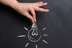 A hand holds a light bulb drawn in chalk on a black chalk board., a Business Photo by ndanko
