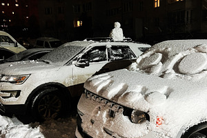 Snowy night in a city parking lot with snow covered cars and glowing apartment, a Photo by AS photostudio