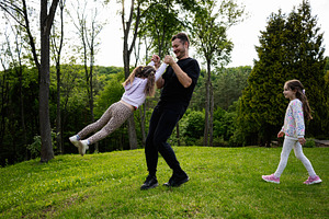 Father playing with daughters in a lush green park setting outdoors, a Person Photo by AS photostudio