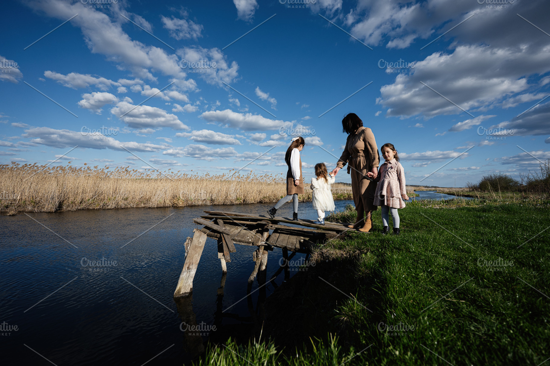 Mother and daughters walking on a rickety wooden bridge by a river in a rural l, a Person Photo by AS photostudio