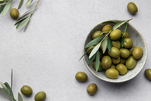 Green olives with leaves served in bowl on concrete table, creat, a Food & Drink Photo by Olena Rudo