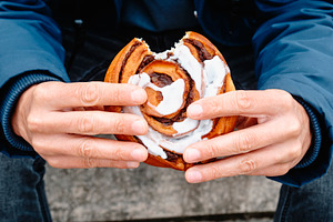 a man holding a bitten danish kanelsnegl on steps, a Photo by Nito