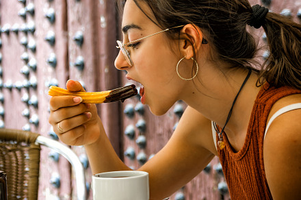Young girl savors a snack of churros and a cup of hot chocolate, an Architecture Photo by Angelo D'Amico Photograph