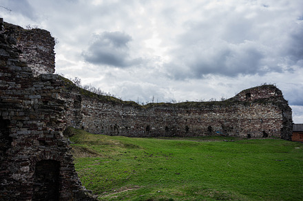 Ancient stone fortress ruins with green grass under a cloudy sky, a Photo by AS photostudio