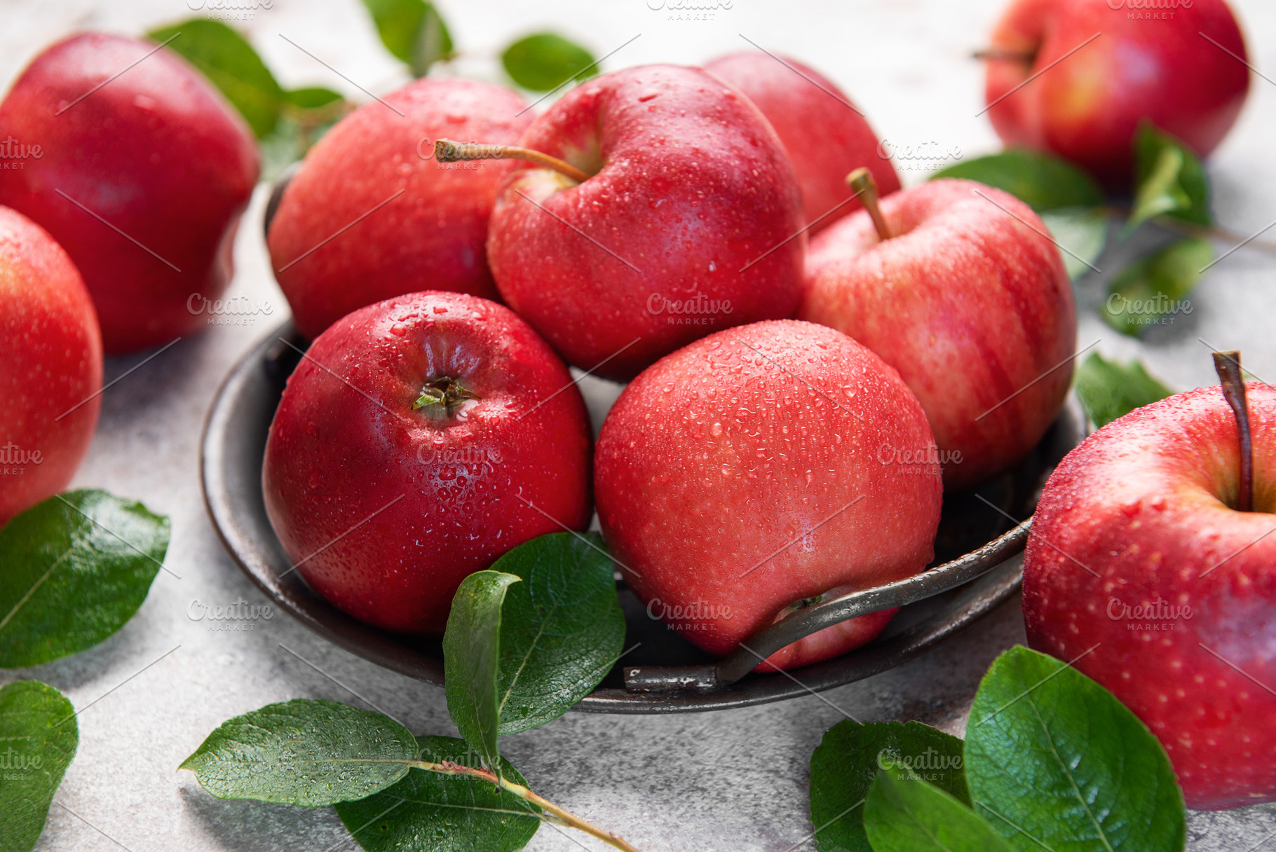 Fresh red apples resting on rustic metal plate with green leaves, a Food & Drink Photo by Olena Rudo