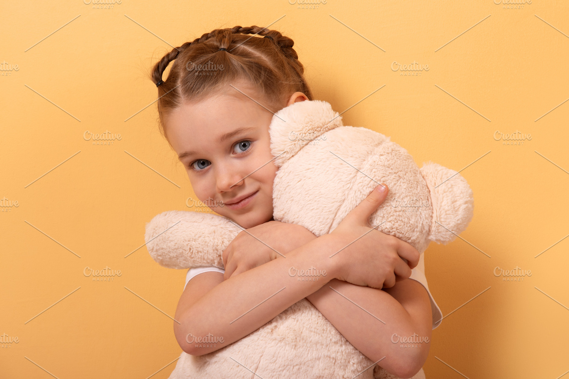 Smiling young girl with braids hugging a large plush teddy bear, a Person Photo by Ales Munt