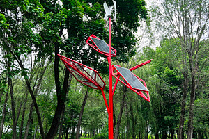 Red solar panel sculpture in park surrounded by lush green trees, a Photo by AS photostudio