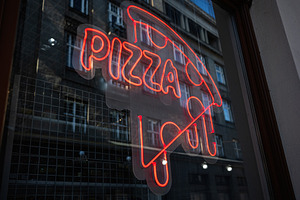 Bright neon pizza sign displayed on urban glass storefront at night, a Photo by AS photostudio