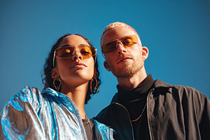 Couple posing in stylish sunglasses against a clear blue sky on a sunny day, a Photo by AlyaAnd