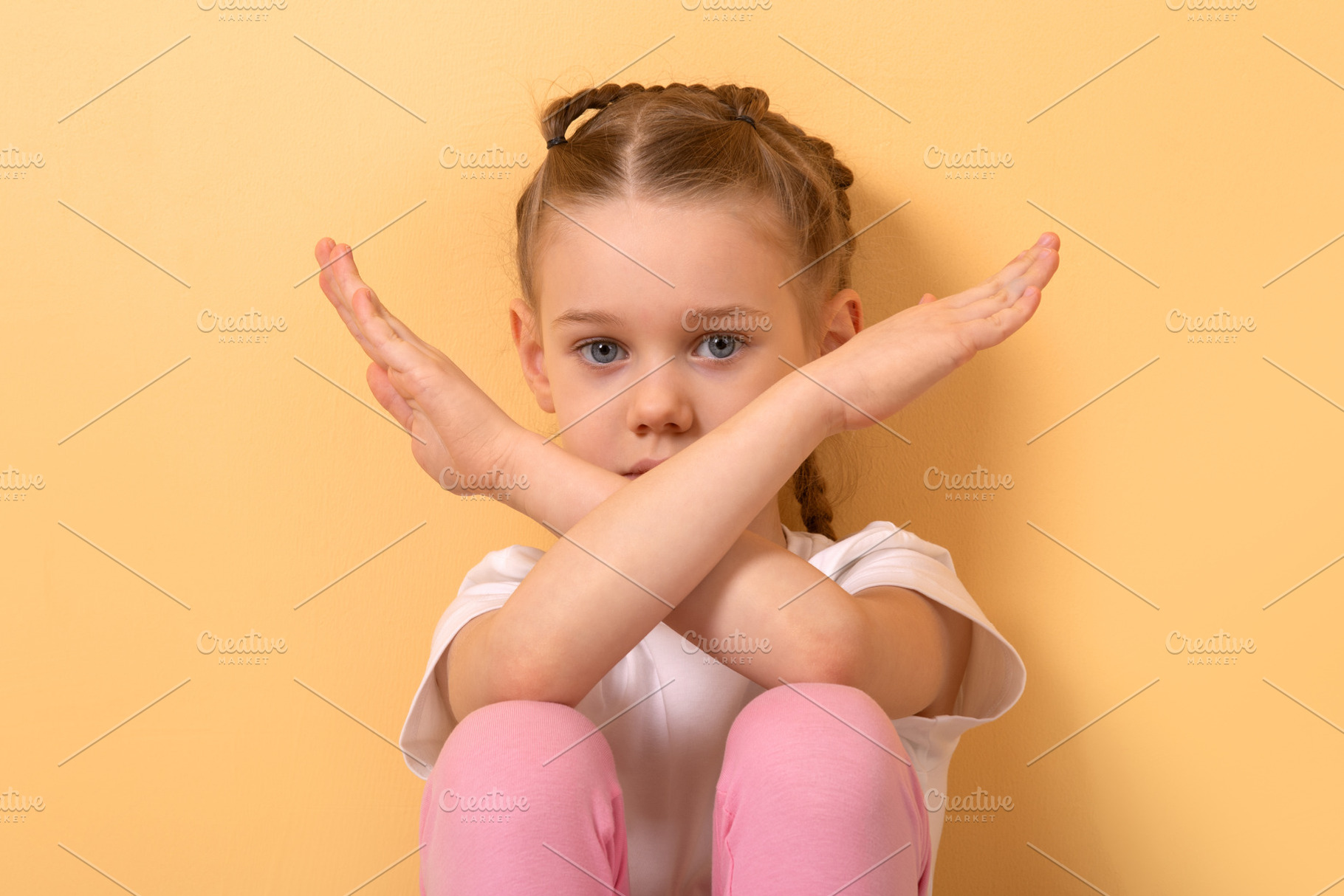 Young girl with braided hair crossing arms in an X sign, seated, a Person Photo by Ales Munt