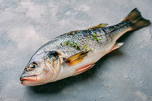 Fresh fish ready for preparation in the kitchen with herbs and spices nearby, a Food & Drink Photo by AlyaAnd