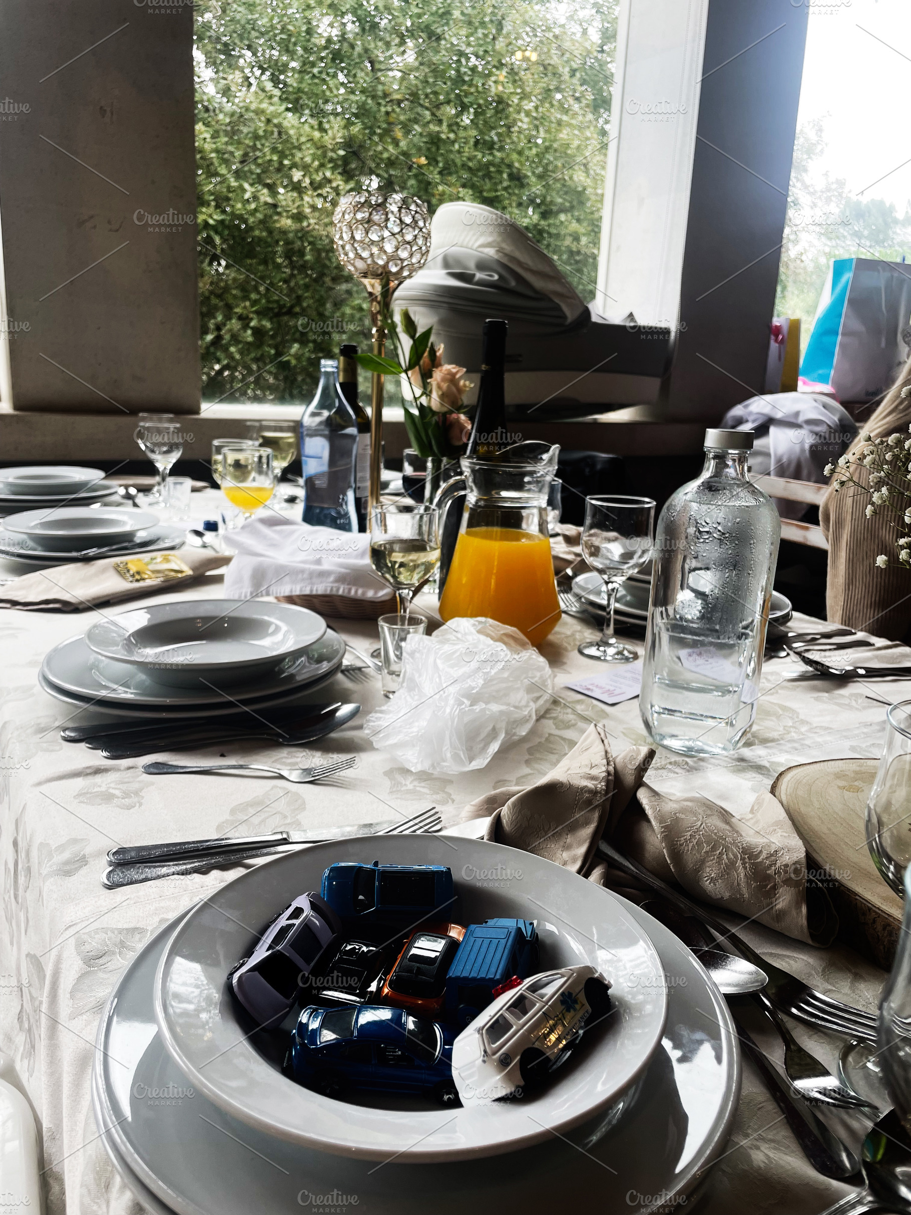 Table setting with dishes, toy cars, and decorations by a bright window, a Photo by AS photostudio