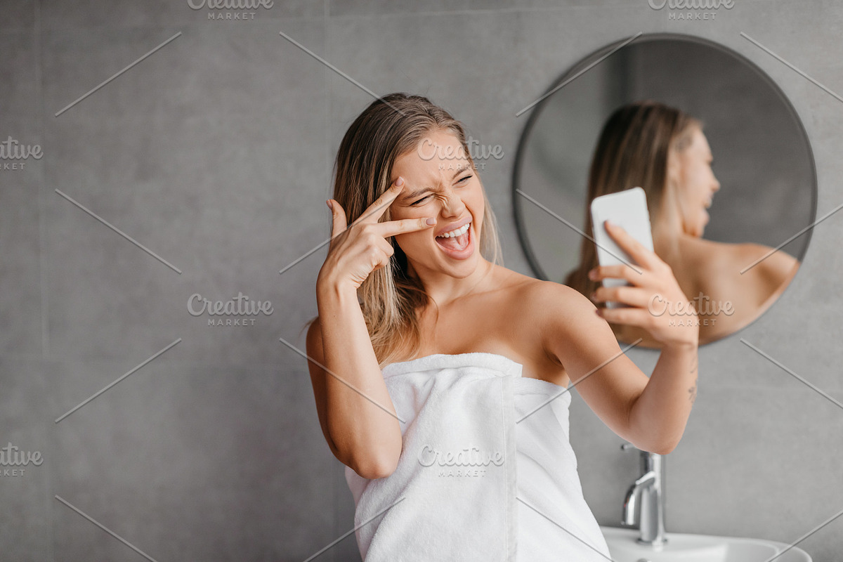 Playful woman taking selfie on smartphone while enjoying beauty morning routine, a Photo by Prostock-Studio (Photo 2 of 3)