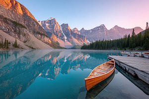 Serene morning at glacial lake with wooden canoe and mountain reflections, a Photo by AlyaAnd