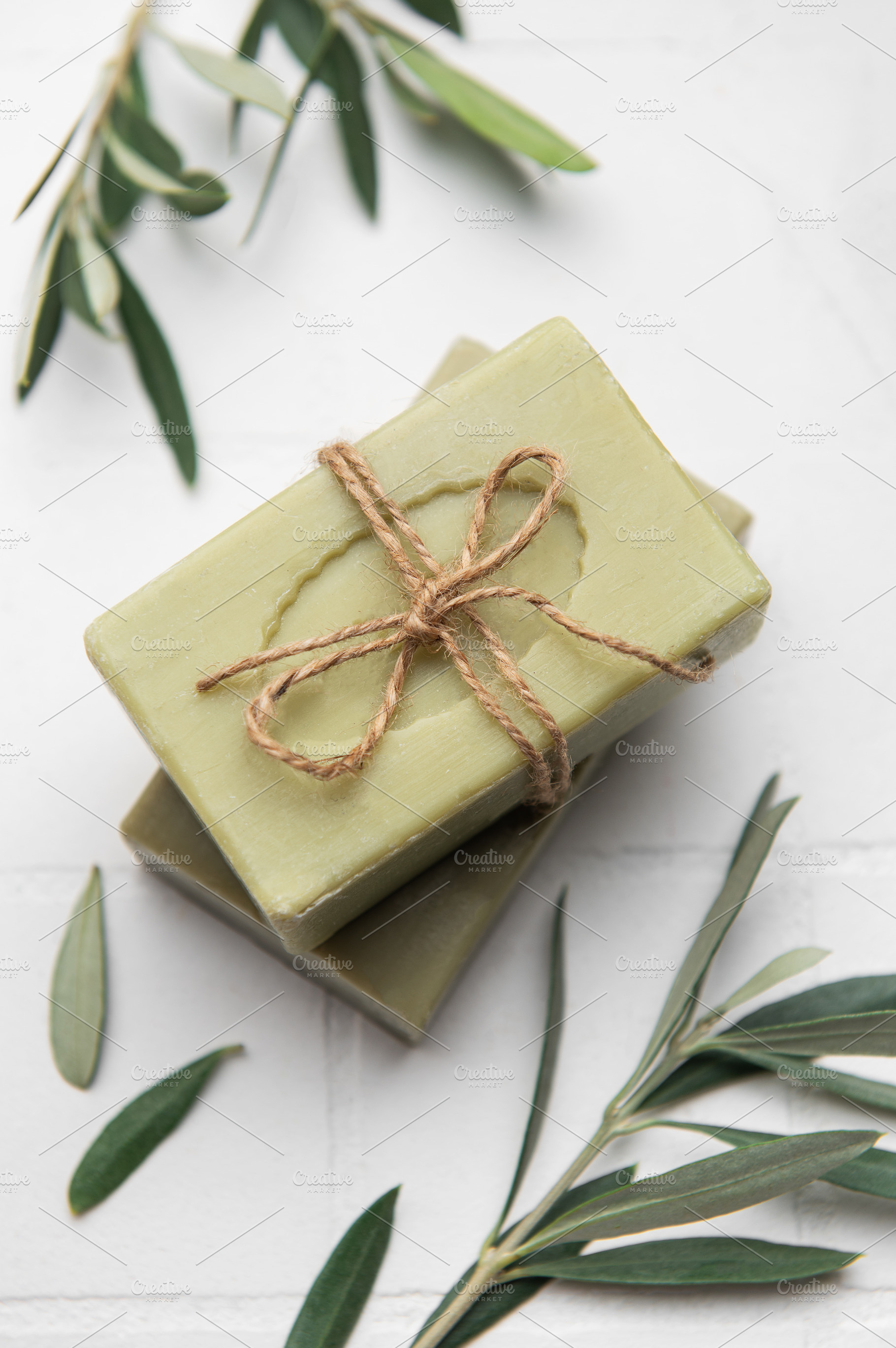 Natural olive soap bars tied with twine on white tile background, a Health & Medical Photo by Olena Rudo