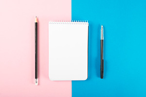 Notebook next to pencil and black pen on pink and blue background. Mockup. Stationery...